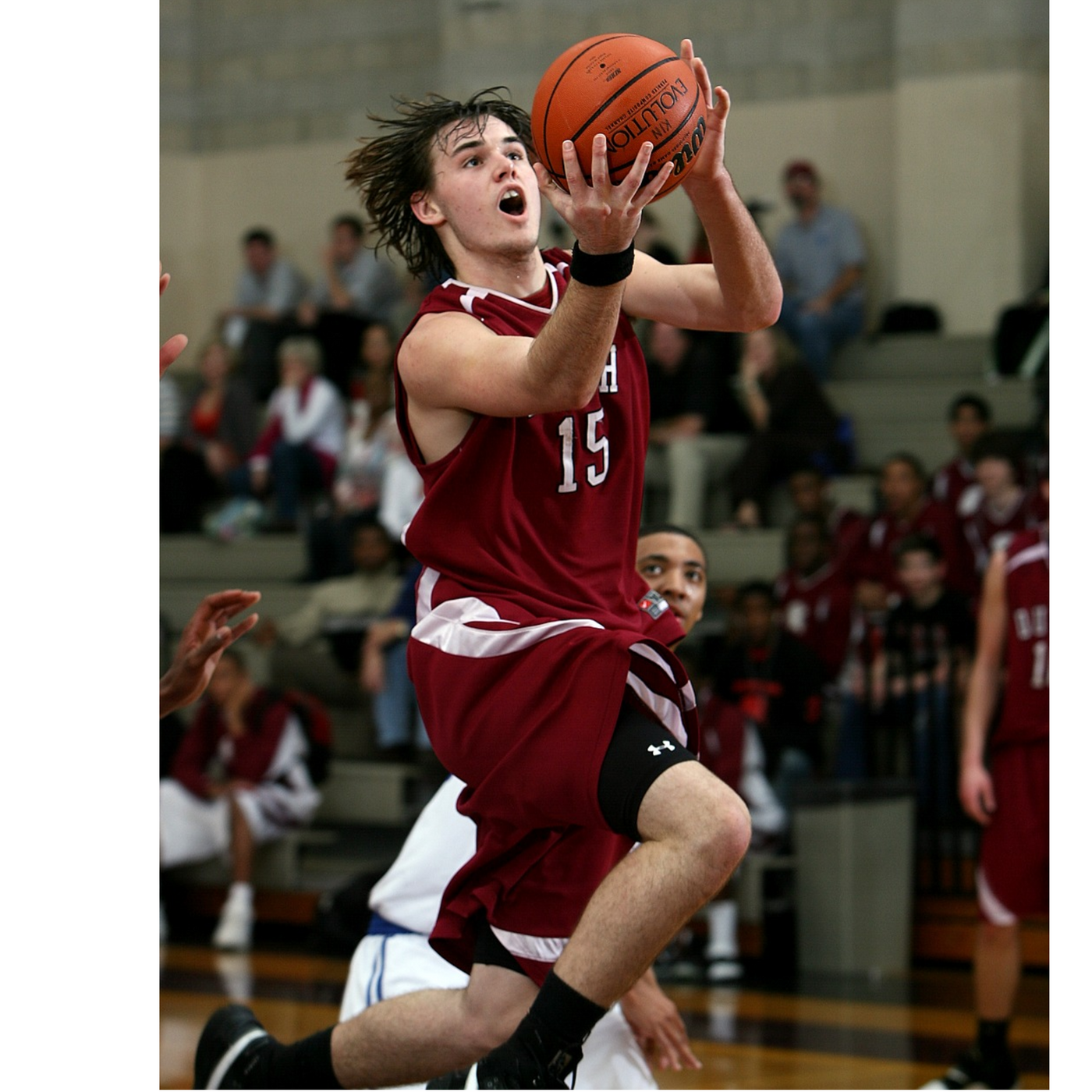 Basketball player in a maroon number 15 uniform jumping toward the hoop for a layup during a game.”